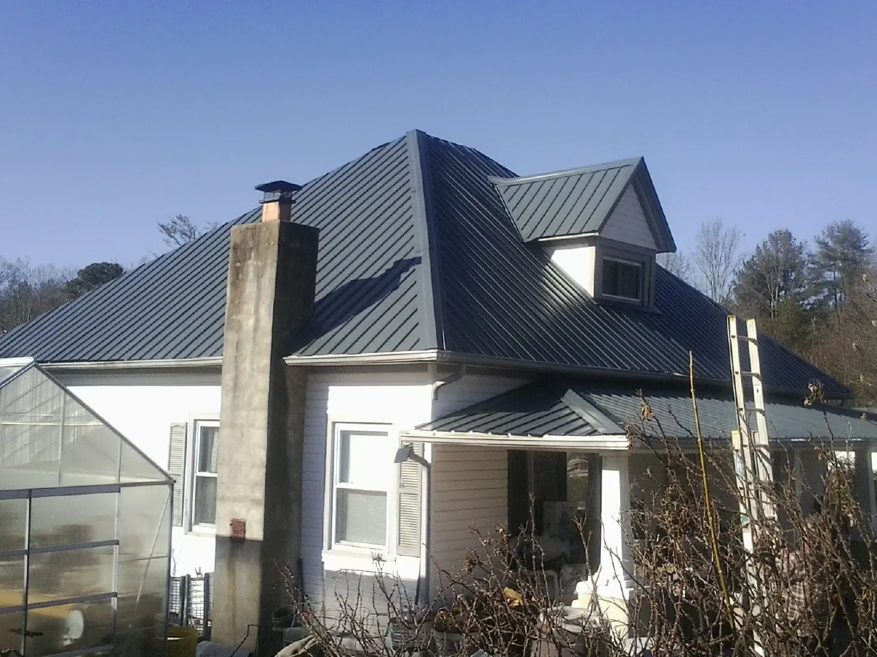 Dark blue standing seam metal roof on a white farmhouse with dormer — Slate & Tile Roof Repair by Roofing Brothers in Elliottsburg