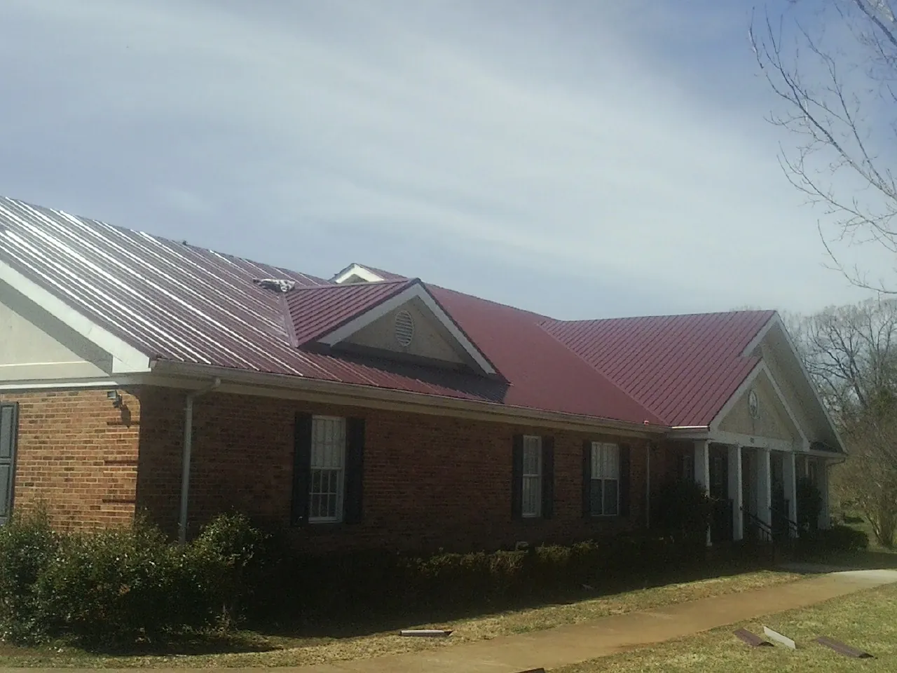 Red metal roof with gabled entries on a long brick building, from a Hail Damage Roof Repair job in Elliottsburg