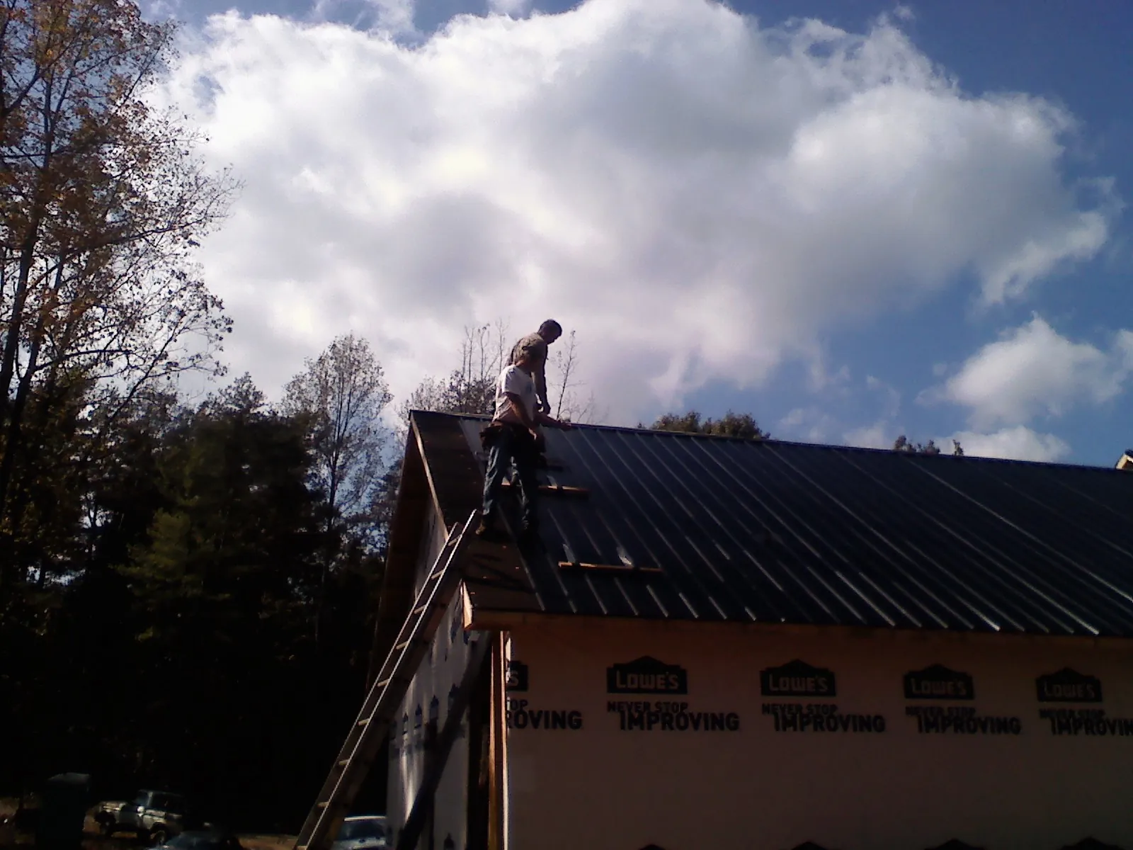 Roofer fastening dark metal panels high against a cloudy sky, from a Roof Inspection job in Elliottsburg