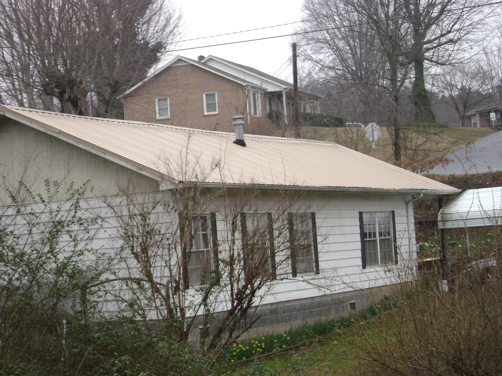 Tan metal roof on a white sided house set into a hillside — Commercial Roofing by Roofing Brothers in Elliottsburg